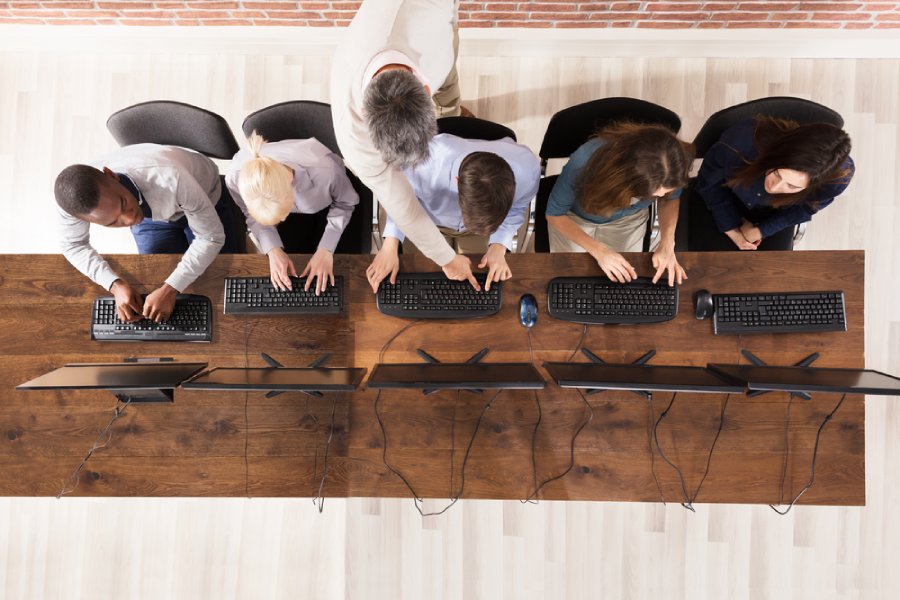 Sesión de formación corporativa en oficina, con varios empleados trabajando en ordenadores mientras un instructor supervisa y les guía